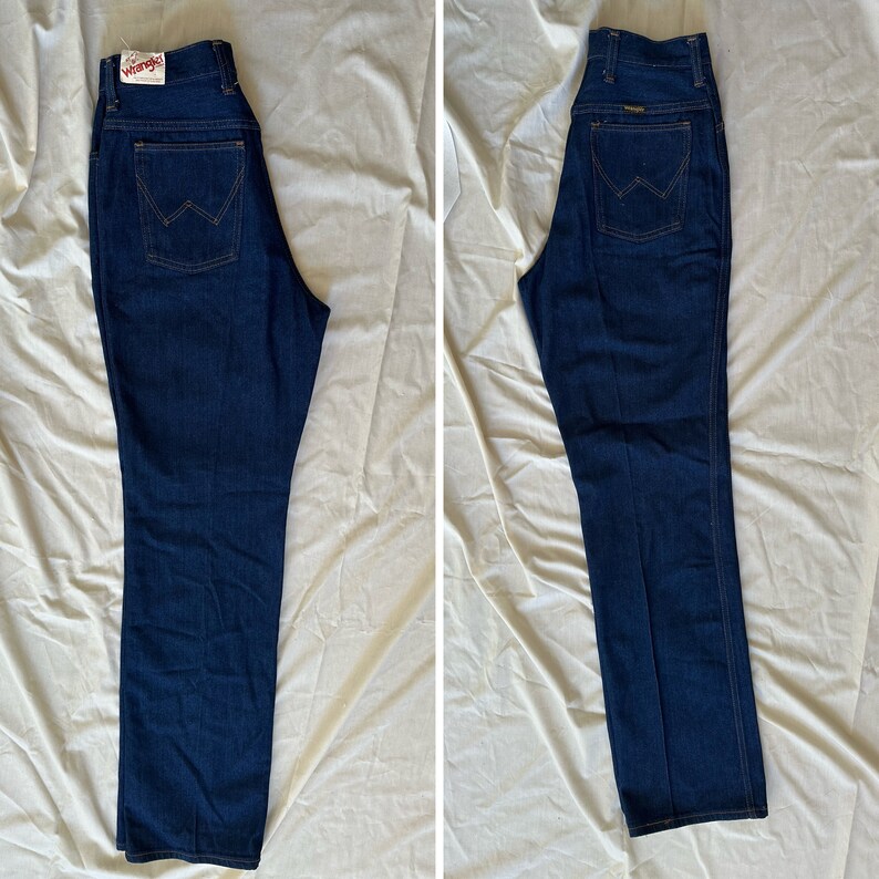 K&ouml;nnte beinhalten: Zwei Paar dunkelblaue Wrangler Jeans. Die Jeans haben ein klassisches F&uuml;nf-Taschen-Design mit geradem Bein. Das Wrangler-Logo ist auf der Ges&auml;&szlig;tasche und auf dem Etikett zu sehen. Die Jeans liegen flach auf einer hellen Oberfl&auml;che.