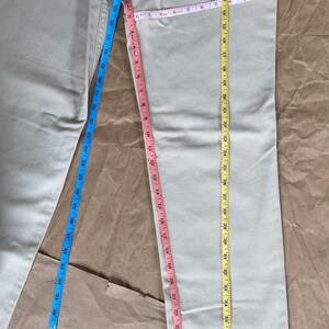 May include: A pair of light beige jeans with a Levi's 511 slim fit straight leg label on the back pocket. The jeans are measured with three tape measures, one blue, one pink, and one yellow.
