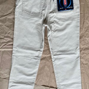 May include: A pair of light beige straight leg jeans with a Levi's 512 slim fit label on the back pocket.