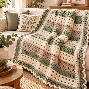 May include: A rectangular crochet blanket featuring alternating horizontal stripes in sage green, cream, and light taupe. The design incorporates open-work grid patterns and textured bobble stitch rows, finished with a scalloped cream crochet border.