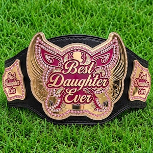 May include: A black leather championship belt featuring a large gold-tone central plate with pink enamel accents and pink rhinestones. The plate displays the text "Best Daughter Ever" in a script font. Two smaller side plates also feature the text.