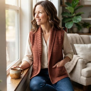 May include: A rust-coloured sleeveless waistcoat featuring a textured waffle-knit pattern, a wide shawl collar, and two front patch pockets. The garment is worn over a light-coloured long-sleeved shirt and blue denim jeans, creating a layered look.