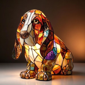 Può includere: Una lampada in vetro colorato a forma di cane Basset Hound. La lampada presenta un mosaico di pezzi di vetro color ambra, marrone, bianco e viola tenuti insieme da linee di metallo scuro. Il cane è seduto con le orecchie lunghe.