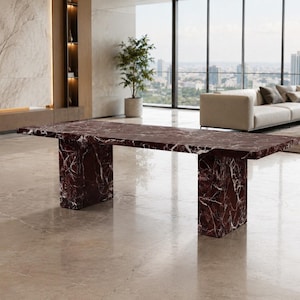 Peut inclure: Une table à manger rectangulaire fabriquée en marbre bordeaux profond avec des veines blanches marquées. La table présente un plateau épais et plat soutenu par deux pieds piédestaux rectangulaires en marbre assortis et massifs.