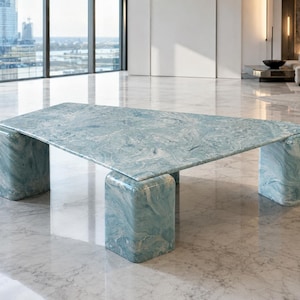 May include: A low coffee table featuring a triangular top and three thick, rounded block legs. The entire structure is finished in a polished, light blue and white marbled pattern with swirling veins throughout the smooth surface.