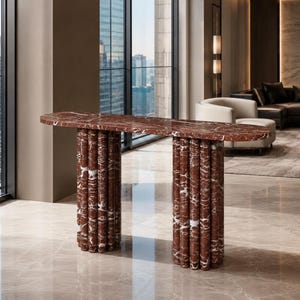 May include: A console table crafted from deep red marble with prominent white veining. The piece features a long, oval-shaped top supported by two substantial bases, each composed of a cluster of vertical, cylindrical marble columns.
