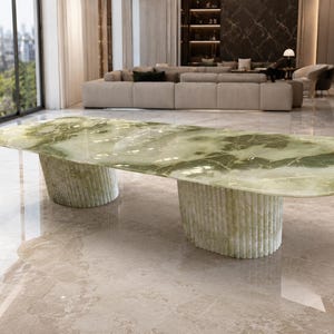 May include: A large dining table featuring a polished, light green marble top with natural white veining. The table is supported by two substantial, cylindrical bases that have a vertical, fluted, or ribbed texture throughout their exterior.