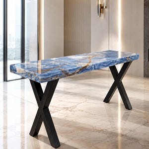 May include: A rectangular console table featuring a polished blue stone top with prominent brown veining. The table is supported by two black metal legs, each designed in a crossed X-shape, providing a stable base for the thick, glossy stone surface.