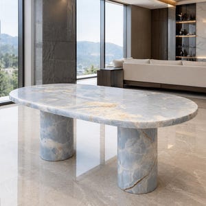 May include: An oval dining table crafted from light blue onyx stone with natural white and gold veining. The tabletop features a smooth, polished surface supported by two thick, cylindrical stone pedestals of the same matching material.