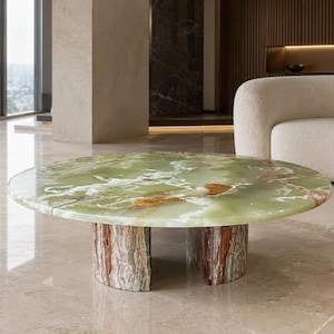 May include: A round coffee table featuring a polished light green onyx top with white and brown veining. The table is supported by two curved, vertical base sections made of a contrasting reddish-brown and green banded stone material.