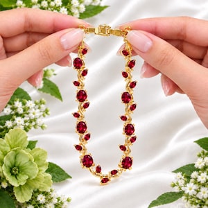 Peut inclure: Un bracelet doré composé d'une série de pierres rouge foncé rondes et en forme de marquise, serties dans une monture métallique en forme de vigne. Le bijou présente un fermoir rectangulaire en haut, reliant deux brins symétriques.