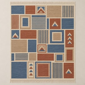 Puede incluir: Una alfombra rectangular con un diseño geométrico de patchwork en tonos azul, terracota y beige. El patrón incluye varios cuadrados y rectángulos con colores sólidos, rayas verticales y pequeños motivos de triángulos escalonados.