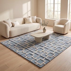 May include: A rectangular area rug featuring a light blue base with a raised, cream-colored geometric grid pattern of interconnected squares. The rug is positioned on a light wood floor, partially underneath a low, light-toned coffee table.