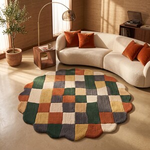 Puede incluir: Una alfombra redonda con bordes festoneados que presenta un diseño de patchwork de bloques rectangulares en tonos verde bosque, naranja quemado, amarillo mostaza, crema y gris carbón, creando un patrón geométrico texturizado y multicolor.