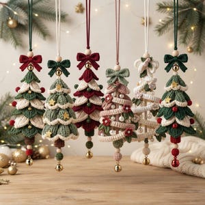 May include: Six hanging Christmas tree ornaments crafted from crochet yarn. Each tree features a unique design with colors including forest green, cream, burgundy, and dusty rose, accented with wooden beads, small bells, and fabric bows.