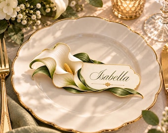May include: A white place card with the name Isabella printed in elegant script, featuring a decorative gold border and a realistic illustration of a white calla lily with green leaves, resting on a white plate with a gold scalloped rim.