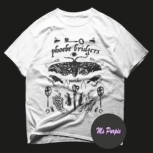 Könnte beinhalten: Ein weißes Kurzarm-T-Shirt mit einem schwarzen Grafikdruck, der einen Nachtfalter, zwei Krähen, Skeletthände, einen Schlüssel und verschiedene kleine Symbole zeigt. Der Text 'phoebe bridgers' und 'punisher' ist in Schwarz aufgedruckt.