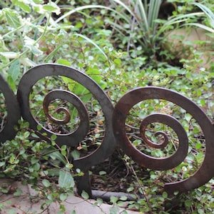 May include: A metal garden border with a decorative spiral design. The border is made of dark brown metal and is shown in a garden setting.