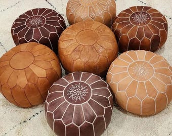 Può includere: Una collezione di sette pouf rotondi in pelle in varie tonalità di marrone, che vanno dal beige chiaro al cioccolato scuro. Ogni pouf presenta un design a pannelli cuciti con un motivo ricamato a forma di stella in filo bianco sulla parte superiore.