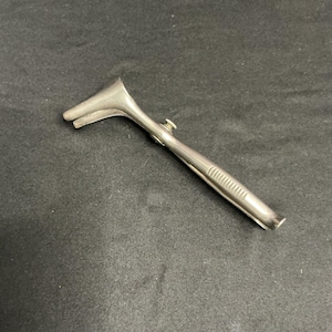 May include: A silver-toned metal nasal speculum featuring a two-pronged tip, a central adjustment screw mechanism, and a textured grip handle. The instrument is constructed from polished stainless steel with a smooth, reflective surface finish.