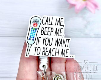 May include: A white badge reel with a retro phone graphic and the text "CALL ME, BEEP ME, IF YOU WANT TO REACH ME...". The badge reel has a clear plastic strap and a metal clip.