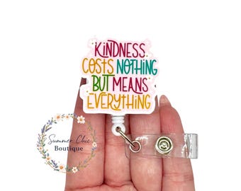 May include: A white badge reel featuring the text "Kindness Costs Nothing But Means Everything" in a rainbow of colours. The reel has a clear plastic strap and a metal clip. The design is on a white background.
