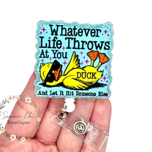 May include: A badge reel with a humorous design. The badge features a yellow cartoon duck wearing sunglasses, with the text "Whatever Life Throws At You, DUCK, And Let It Hit Someone Else." The badge has a glittery blue border and a clear plastic reel.