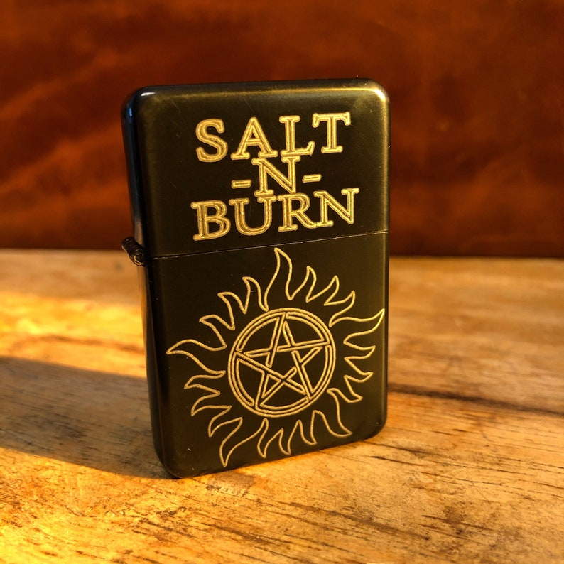 May include: Black lighter with a gold inscription that reads "SALT -N- BURN" and a gold pentagram with flames around it.
