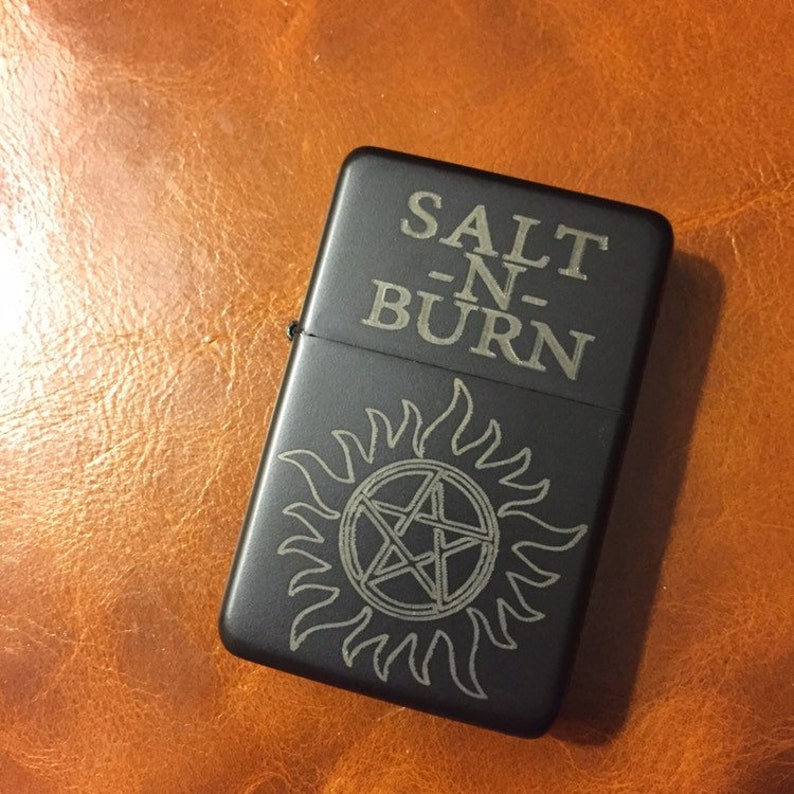 May include: Black lighter with a silver engraved design of a pentagram inside a circle with flames. The text "SALT -N- BURN" is engraved above the design.