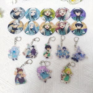 May include: A collection of ten circular pin-back buttons and eight acrylic keychains featuring anime-style character illustrations. The buttons display individual portraits with names like Qifrey, Richeh, Coco, Tetta, and Agott. The keychains show various character pairs and solo figures in colorful outfits.