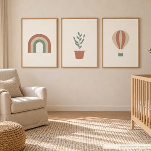 May include: Three framed wall art prints displayed in a row. The left print features a muted rainbow, the center print shows a potted plant, and the right print depicts a hot air balloon. Each illustration uses a soft, earthy color palette.