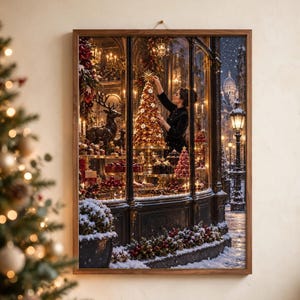 May include: A framed wall art print depicting a storefront window display at night during winter. Inside, a person places a star atop a golden Christmas tree surrounded by pastries and a reindeer statue. Snow falls on the street outside.
