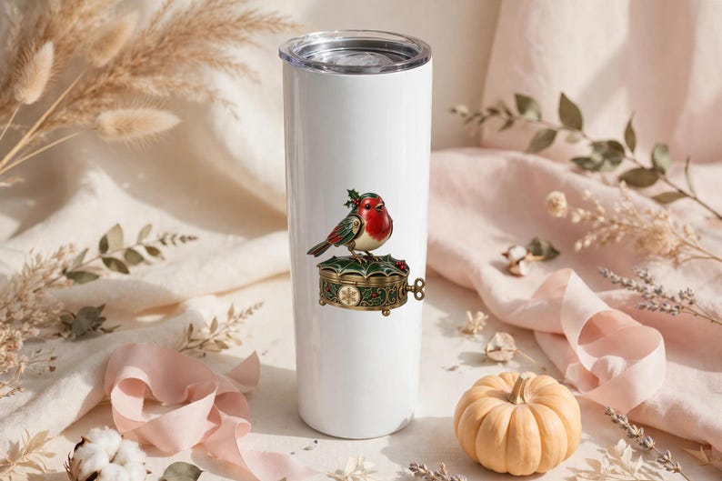 May include: A white cylindrical tumbler with a clear lid featuring a graphic of a red-breasted robin perched on a decorative, ornate, dark green and gold trinket box adorned with holly leaves and a small snowflake pattern.