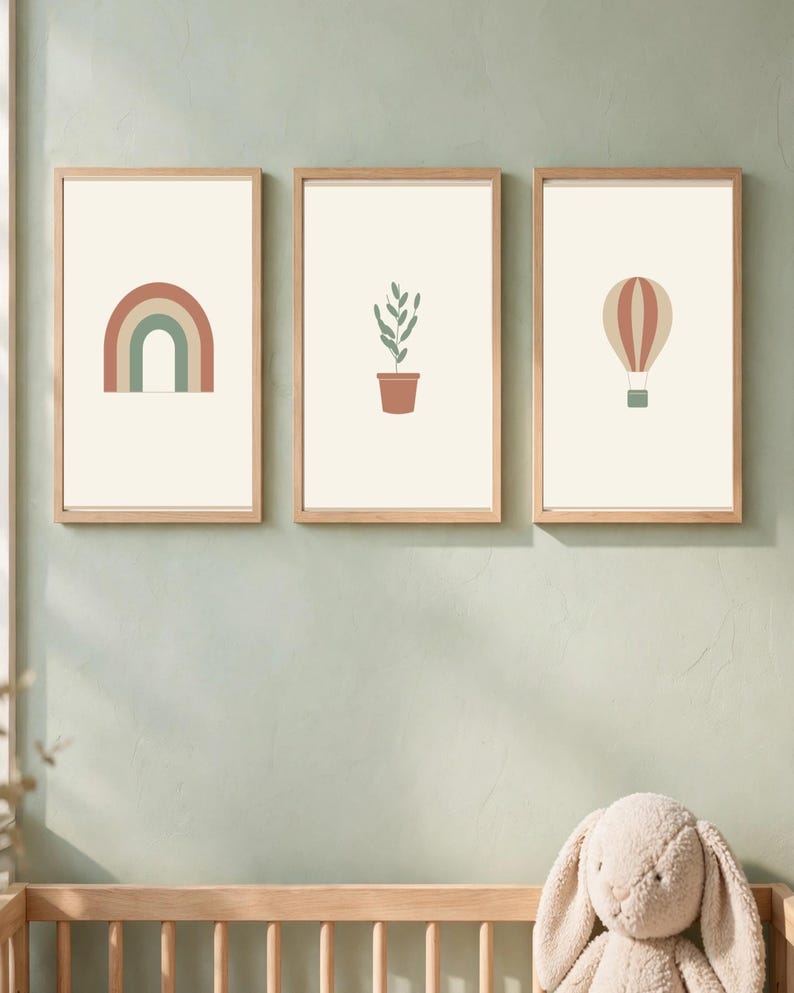 May include: Three framed wall art prints with light wood frames. The left print features a rainbow in muted red and green. The center print shows a green potted plant. The right print displays a hot air balloon in red and beige tones.