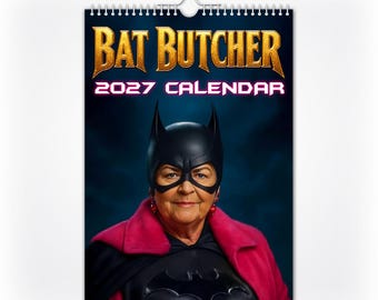 Op de afbeelding: Een wandkalender voor 2027 met de titel Bat Butcher, met een portret van een persoon die een zwart vleermuismasker en een felroze cape over een zwart pak draagt. De tekst Bat Butcher 2027 Calendar staat in grote gouden en witte letters gedrukt.