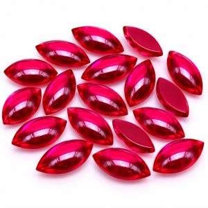 May include: A collection of numerous marquise-cut, translucent red gemstones. Each stone features a smooth, polished surface with a pointed oval shape, reflecting light to create deep crimson highlights across the faceted glass-like material.
