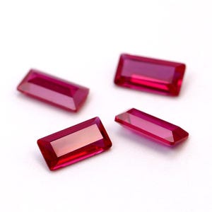 May include: Four loose, rectangular, baguette-cut gemstones with a vibrant, deep magenta-red color. Each stone features faceted surfaces that reflect light, creating a clear, transparent appearance with sharp, defined edges and a polished finish.