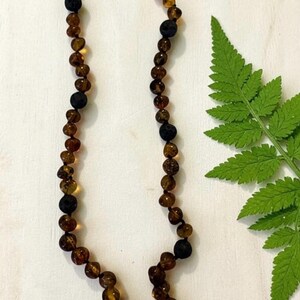 May include: A necklace featuring a series of translucent, honey-colored amber beads interspersed with matte black, porous lava stone beads. The beads are strung together on a dark cord, creating a repeating pattern of smooth and textured elements.