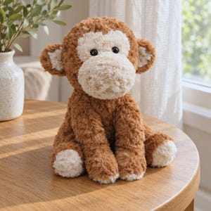 May include: A plush monkey toy with brown, textured fur and a cream-colored face, ears, and paws. The stuffed animal features round black eyes and a soft, rounded snout, sitting in an upright position with its arms resting at its sides.