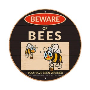 Può includere: Un cartello rotondo nero con un ovale rosso in alto contenente il testo BEWARE OF BEES. Sotto, il testo recita YOU HAVE BEEN WARNED NOT RESPONSIBLE FOR INJURY OR DEATH. Il centro presenta due api disegnate su uno sfondo in legno chiaro.
