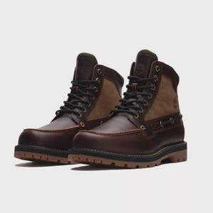 Puede incluir: Un par de botas de cuero marrón oscuro con diseño de puntera tipo mocasín, paneles laterales de ante color tostado, cordones negros y ojales metálicos. Las botas tienen una suela de goma gruesa y estratificada con un logotipo grabado.