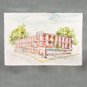 May include: Watercolor painting of a red brick hotel on a corner lot. The word "HOTEL" is on the roof. A sign that says "Cafe" is visible. Green trees and a light post are in the scene. The artwork is on a white paper with a gray background.