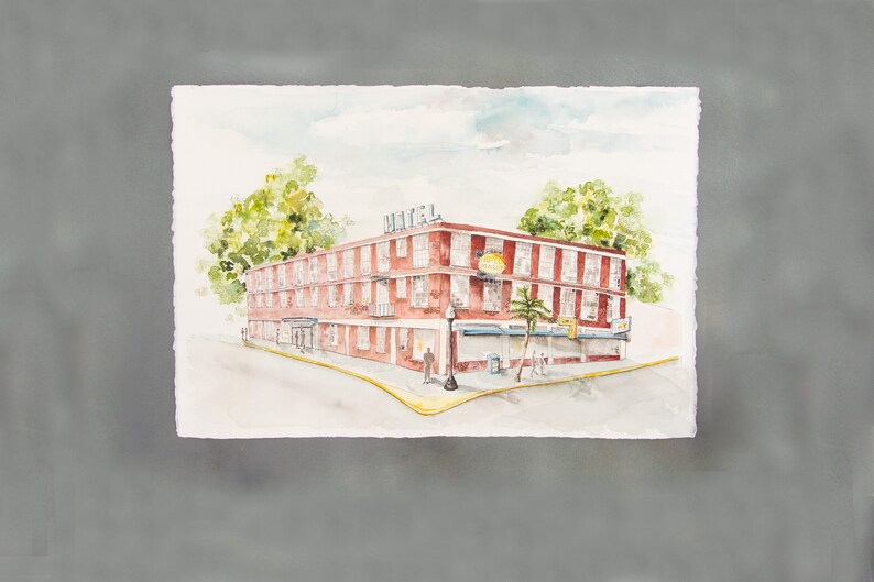 May include: Watercolor painting of a red brick hotel on a corner lot. The word "HOTEL" is on the roof. A sign that says "Cafe" is visible. Green trees and a light post are in the scene. The artwork is on a white paper with a gray background.