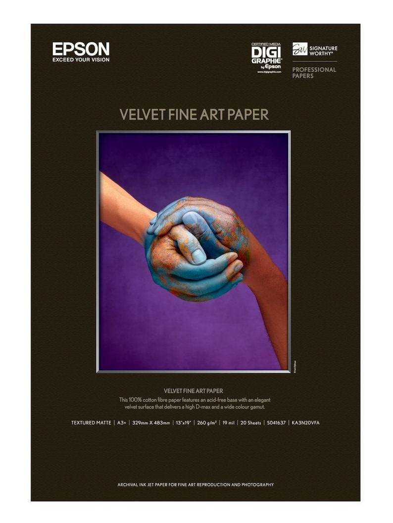 May include: Epson Velvet Fine Art Paper. The image shows a close-up of two hands, one painted blue and the other orange, clasped together against a purple background. The paper is textured matte, 13" x 19".