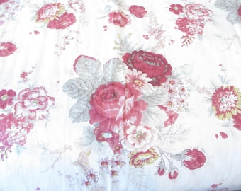 May include: A white fabric featuring a repeating floral pattern with deep red roses, pink blossoms, and muted sage green leaves. The design includes clusters of various flowers scattered across the surface, creating a dense botanical print.