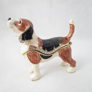 May include: A decorative dog figurine in a standing pose, featuring a white, brown, and black color scheme. The figurine is adorned with gold accents and sparkling rhinestones. The dog's tail is raised, and it appears to be looking upwards.