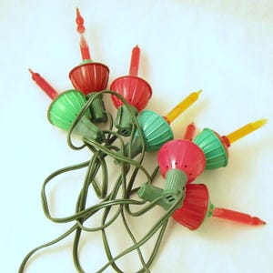May include: A cluster of vintage Christmas lights with red, green, and yellow bulbs. The bulbs have a classic, round shape with a pointed top. The lights are connected by a green wire.