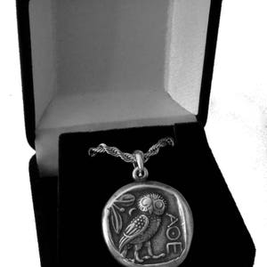 May include: Silver-toned pendant necklace featuring a detailed owl design within a circular frame. The pendant is displayed in an open black velvet jewelry box. The owl is depicted with intricate details, and the necklace chain is visible.