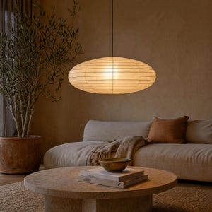 May include: A large, oval-shaped pendant light with a ribbed, off-white paper shade suspended by a thin black cord. The light emits a warm, soft glow, illuminating the horizontal paper texture and the delicate structure of the lamp shade.