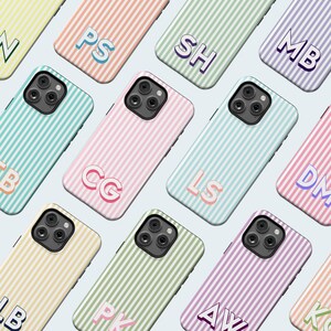 May include: A collection of colorful phone cases with a striped pattern and personalized initials. The cases are in various pastel colors, including pink, green, and yellow. Each case has a different set of initials in a matching color.